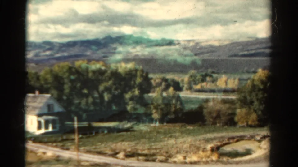 1967 Colorado 8mm frame with a small farmhouse, rural fields, autumn trees and distant mountains under clouds.