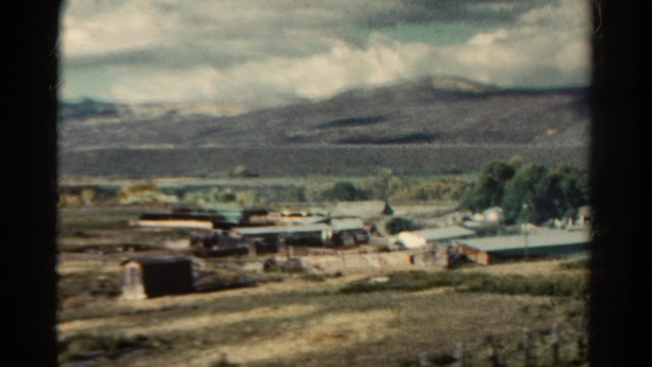 Low rural buildings and open fields with mountains in the distance.