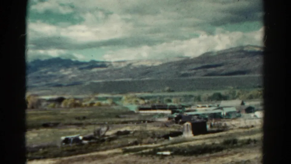 1967 Colorado 8mm frame showing rural buildings, open land, tree clusters, and mountains with visible film gate edges.