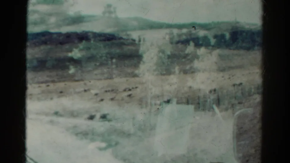 1967 Colorado 8mm frame showing dry open land, distant pine trees, fencing, and soft reflections across the film image.