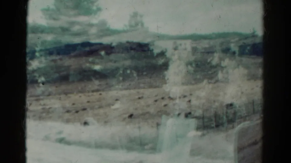 1967 Colorado home-movie frame with a dry field, distant trees, low terrain, fence posts, and vehicle-window reflections.