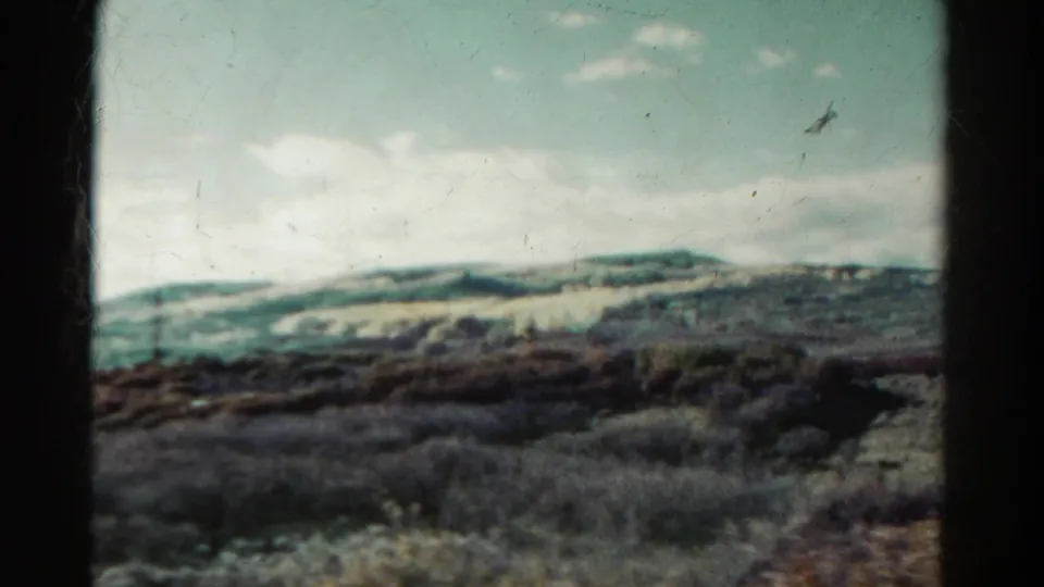 1967 Colorado 8mm frame showing distant hills and mountain ridges beyond dark brush and sparse vegetation.