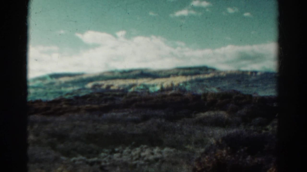 Rolling hills and clouds with a dark foreground band and a small speck in the sky.