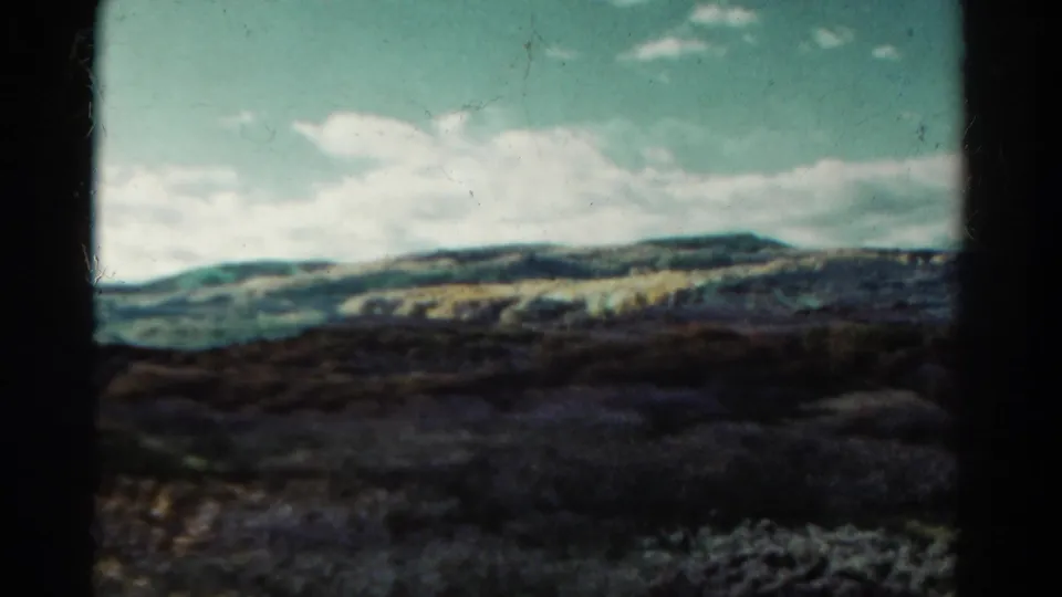 1967 Colorado 8mm frame showing a mountain horizon, broken clouds, and shadowed brush in the foreground.