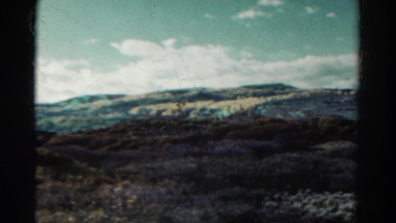 Rolling foothills and scrubby shrubs beneath a pale blue sky with white clouds.