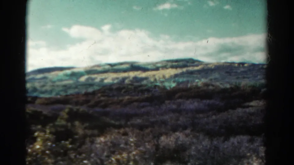 1967 Colorado 8mm view of a brushy foothill landscape, with muted color, soft focus, and clouds stretching across the sky.