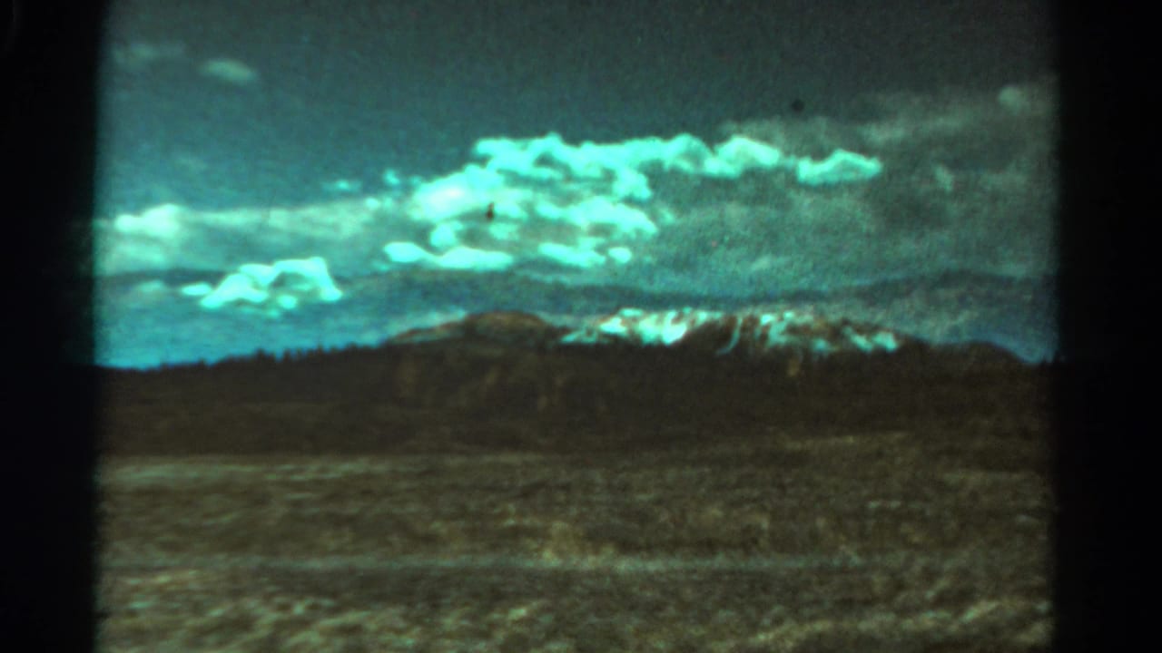 Distant mountains and low hills beyond an open plain under a bright cloud band.