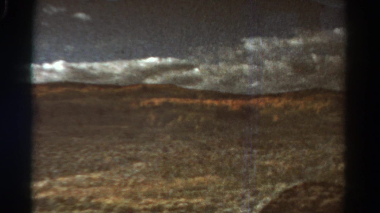 Dark window framing an open valley with distant hills and grey cloud cover.