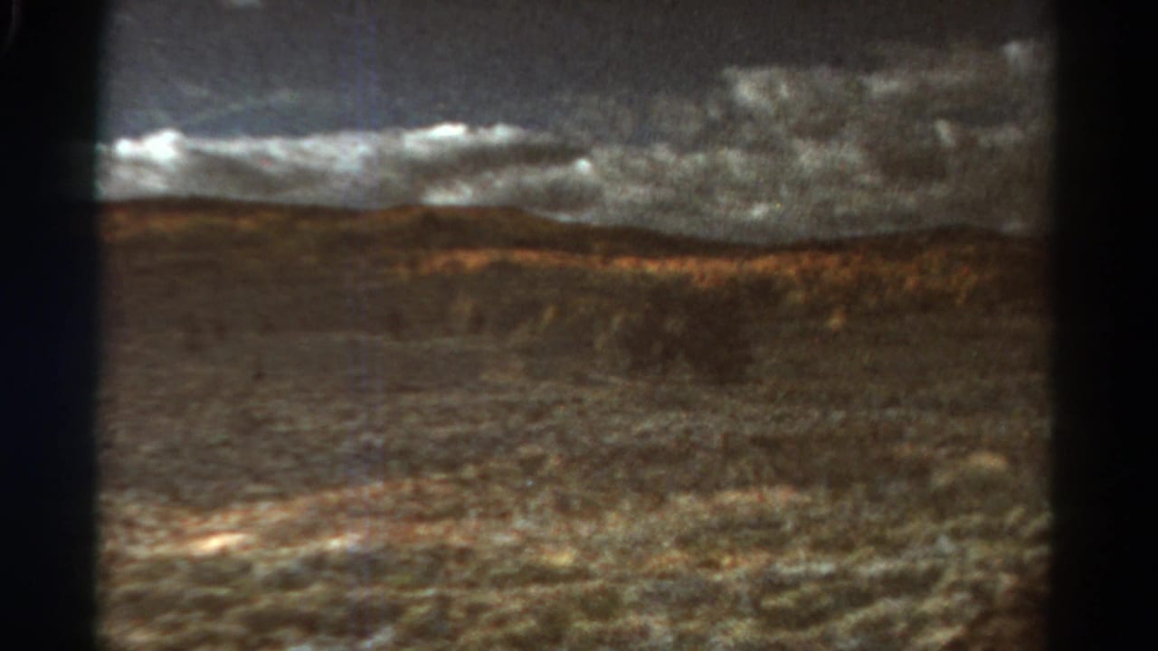1967 Colorado train-view frame with dark window bars dividing a hazy valley, distant hills, and a layered grey sky.