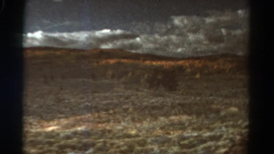 1967 Colorado train-view frame with dark window bars dividing a hazy valley, distant hills, and a layered grey sky.