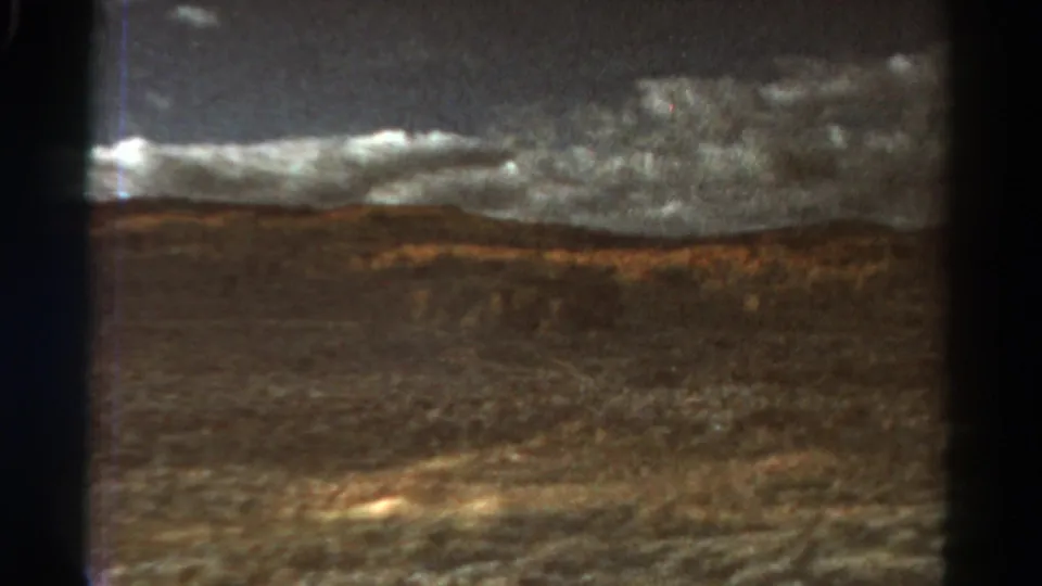 1967 Colorado 8mm frame showing arid valley ground, low hills, and dense cloud cover from a moving train viewpoint.