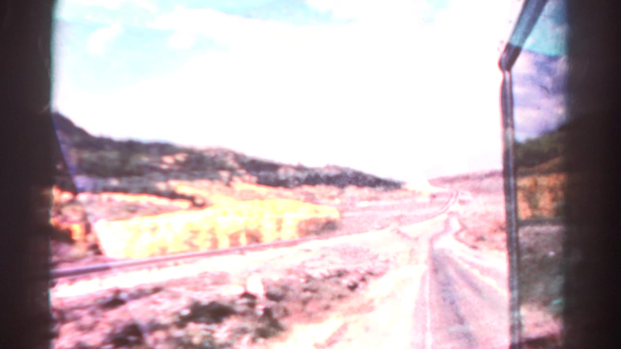 Roadside mountain view with railroad tracks, autumn trees, and dark frame edges.