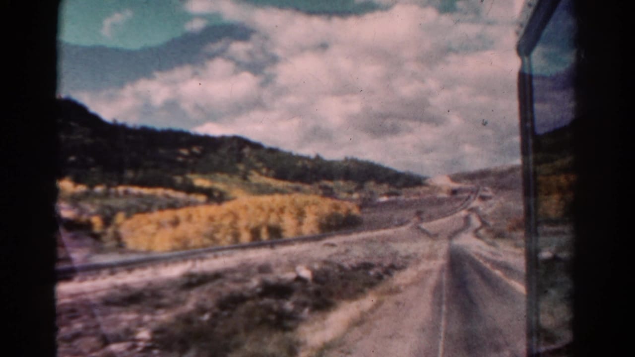 Winding road and railroad tracks pass through a mountain valley under clouds.