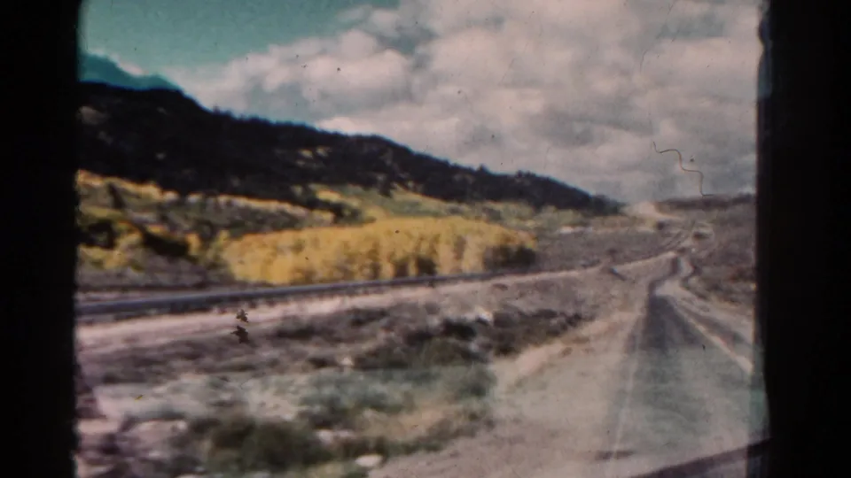1967 Colorado 8mm frame with railroad tracks, a roadside edge, golden trees, wooded hills, and visible home-movie grain.