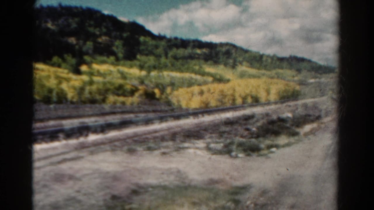 Parallel railroad tracks run past golden trees and dark mountain slopes.