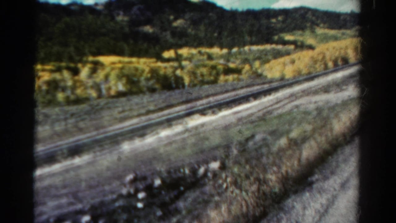 Railroad tracks and a roadside valley below wooded hills.