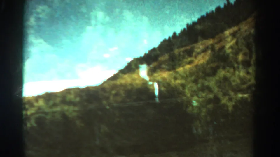 Soft 8mm Colorado mountain view with a steep hillside, bright clouded sky, and blurred roadside landscape.