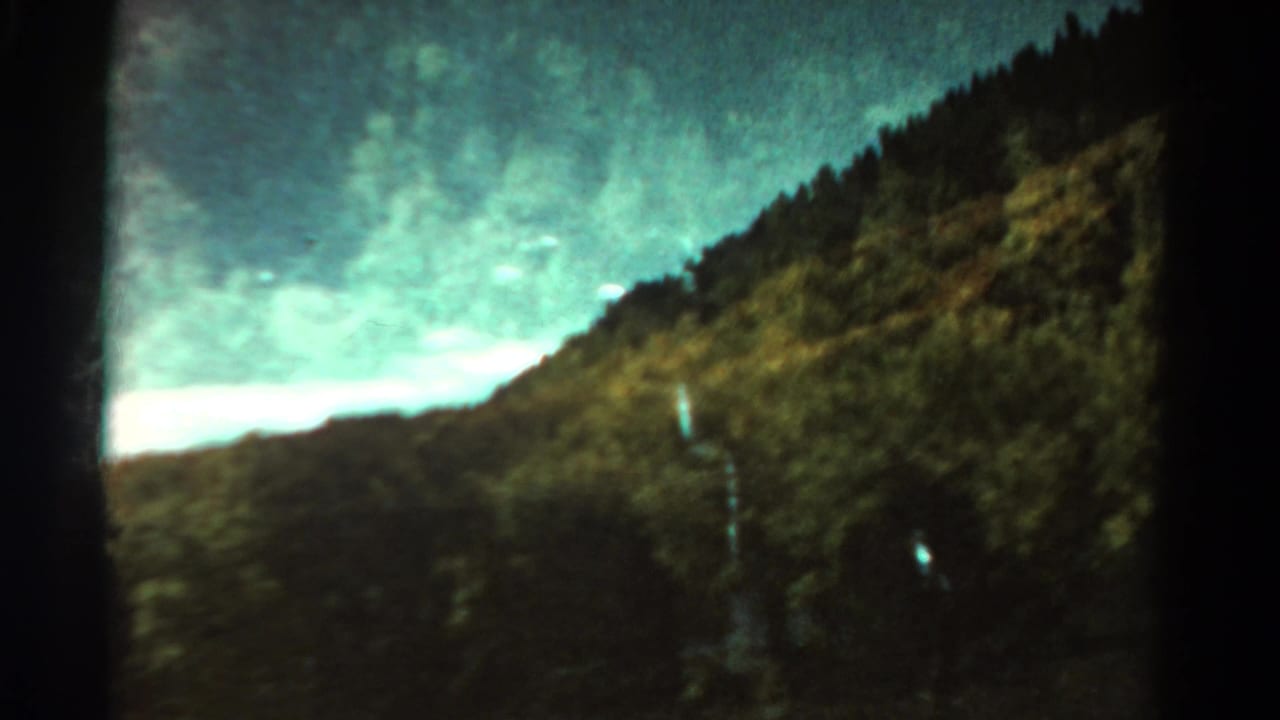 Wooded mountain slope beneath a pale sky with dark film frame edges.