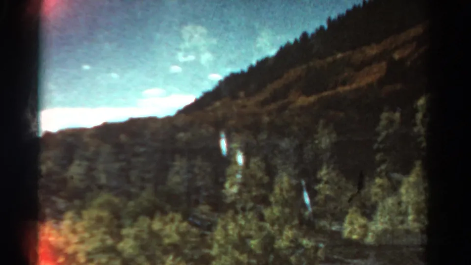 Colorado 8mm home-movie view of a forested mountain slope, distant ridge line, and blue-green sky from 1967 metadata.