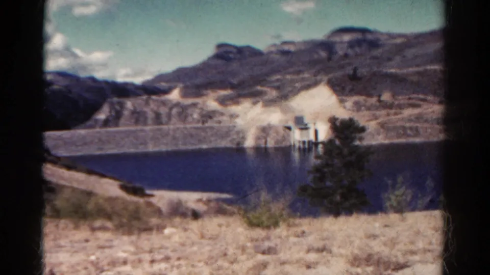 Colorado reservoir and dam landscape filmed on 8mm, with arid foreground grasses and layered rocky slopes beyond the water.
