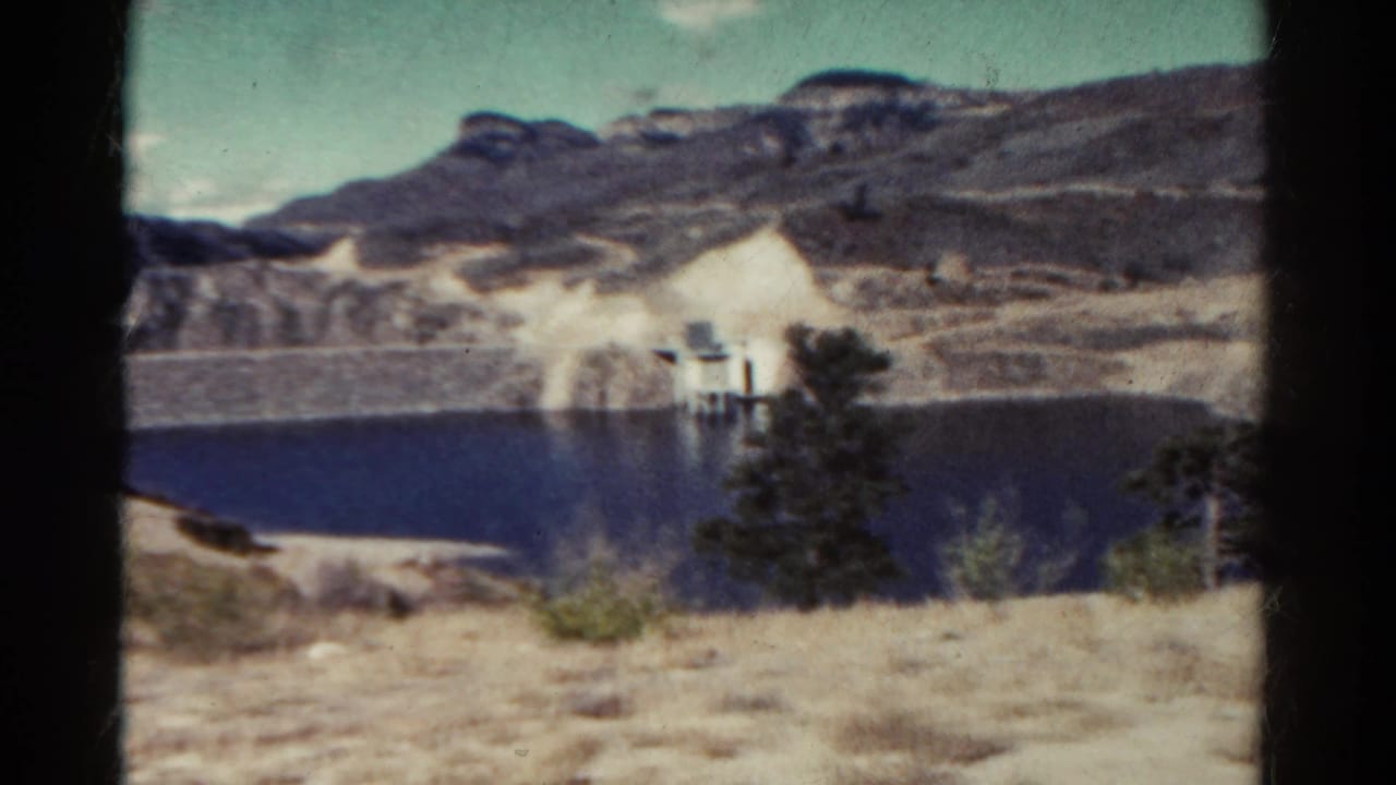 Lake and rocky hillside with a small lakeside structure partly framed by dark film edges.