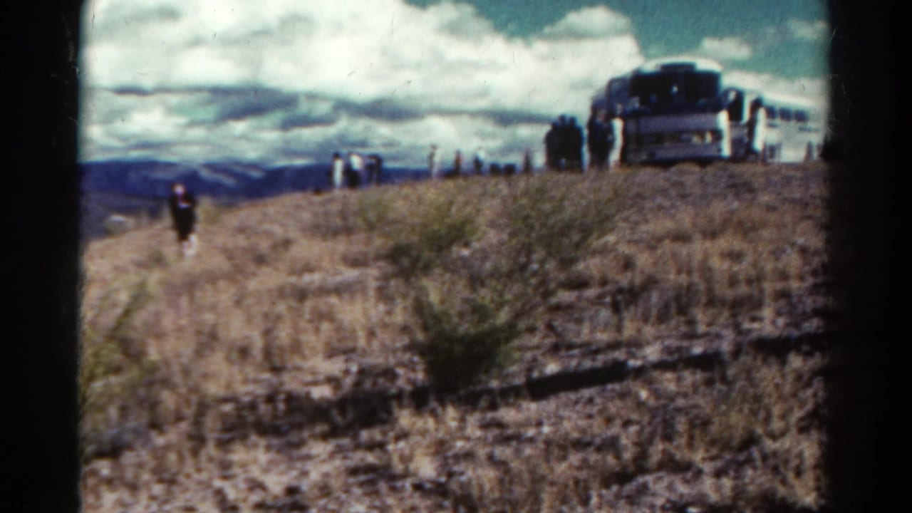 Tour bus and visitors on a dry hillside under a cloudy sky.