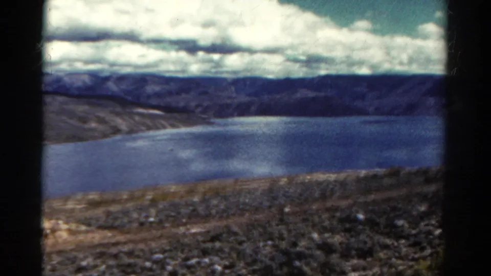 Wide 1967 Colorado travel view of a large lake bordered by mountains and dry shoreline beneath a cloud-filled sky.