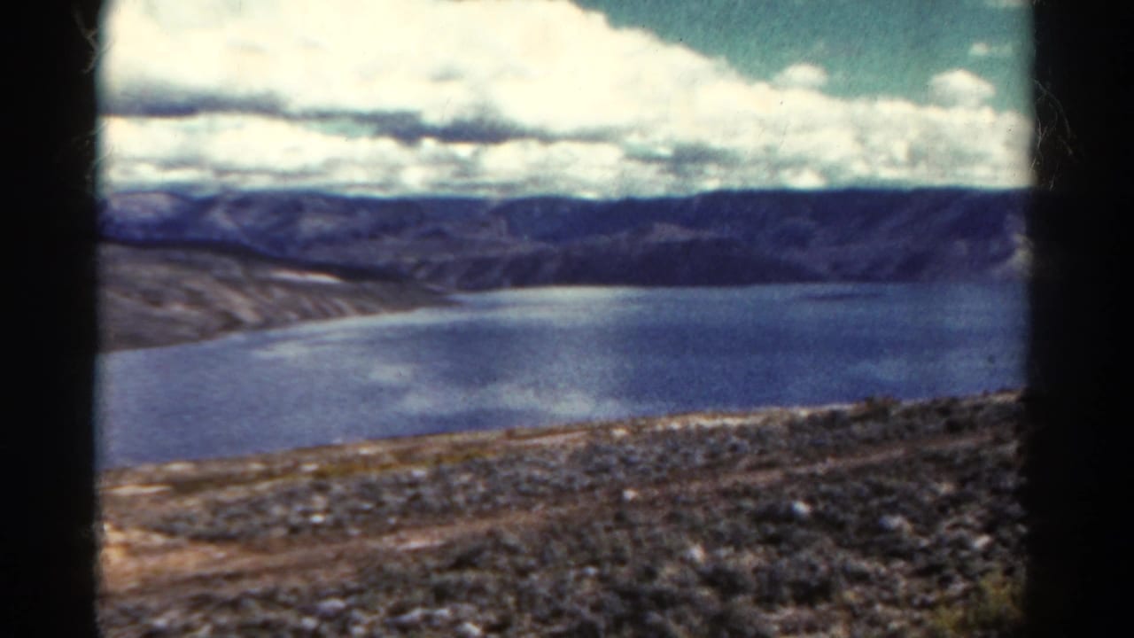 Elevated view across a blue lake toward dark hills under a cloudy sky.
