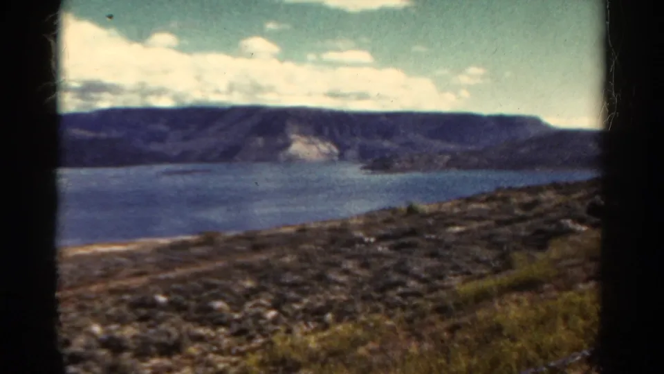 1967 Colorado home-movie frame of a rocky hillside above a blue lake, with distant ridges and soft 8mm color.