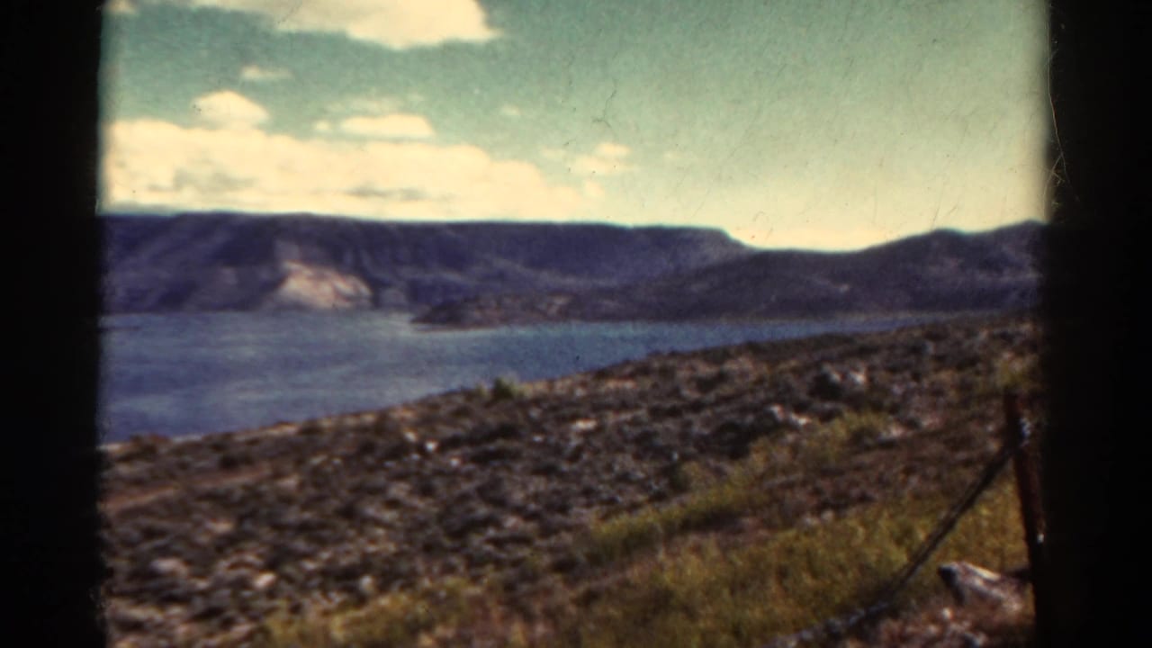 Lake and mountain ridge under a pale sky, framed by dark film edges.