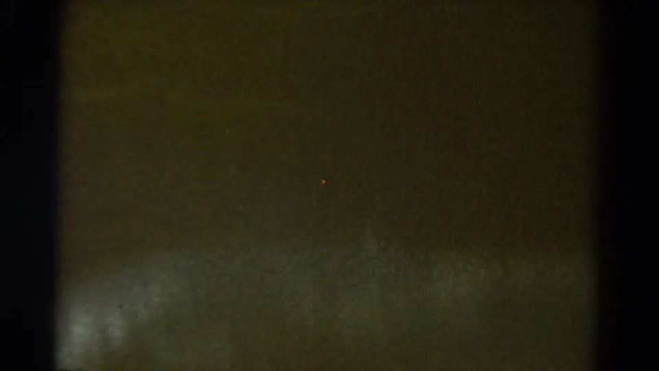 Dark transitional 8mm frame with faint blurred texture near the bottom, likely the camera ending the landscape shot.