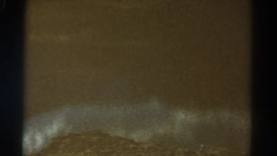 End frame from the 1967 8mm clip, showing a dark close-up with faint pale texture and visible film grain.