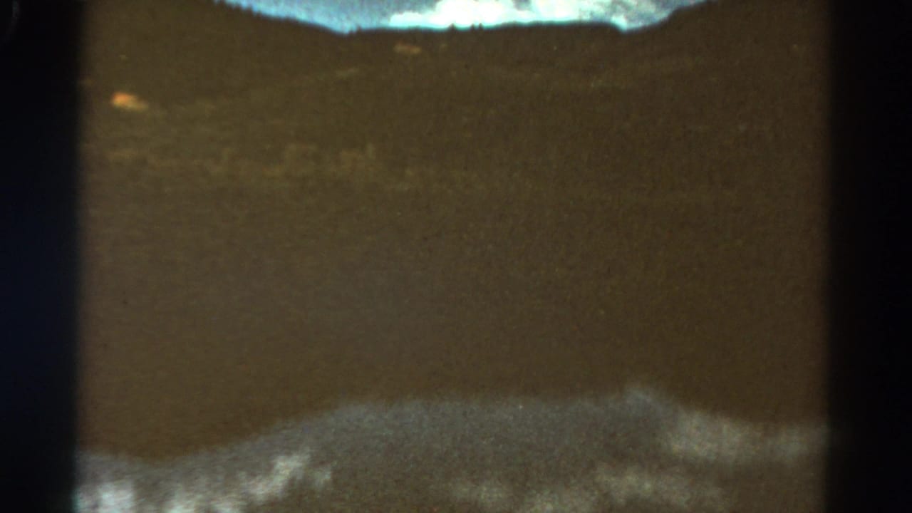 Still water and distant hills framed by dark vertical film edges and a pale strip of sky.