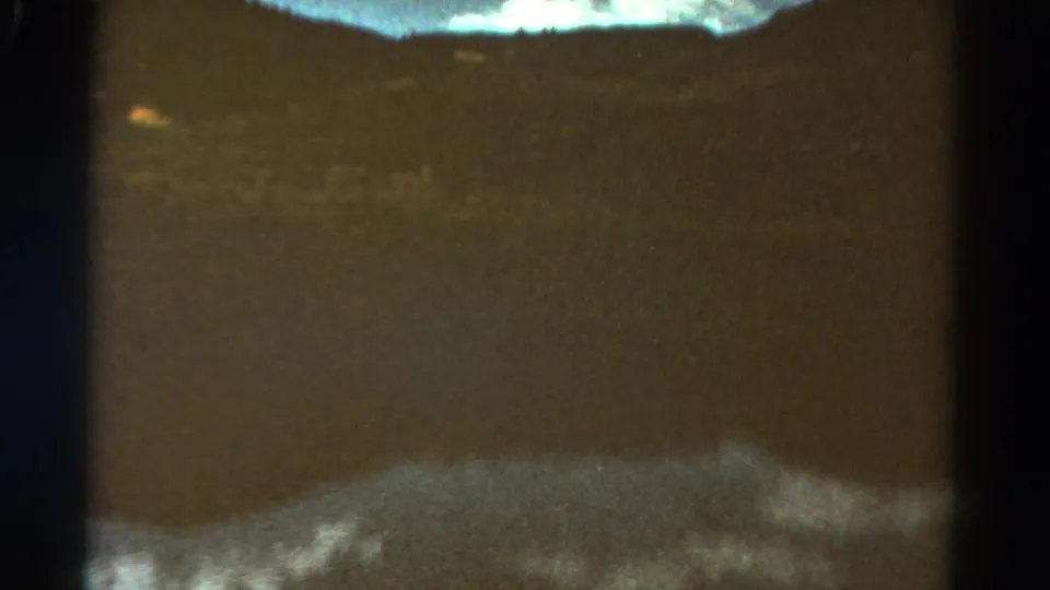 1967 Colorado 8mm frame with calm water in the foreground, low hills beyond, and visible film gate shadows.
