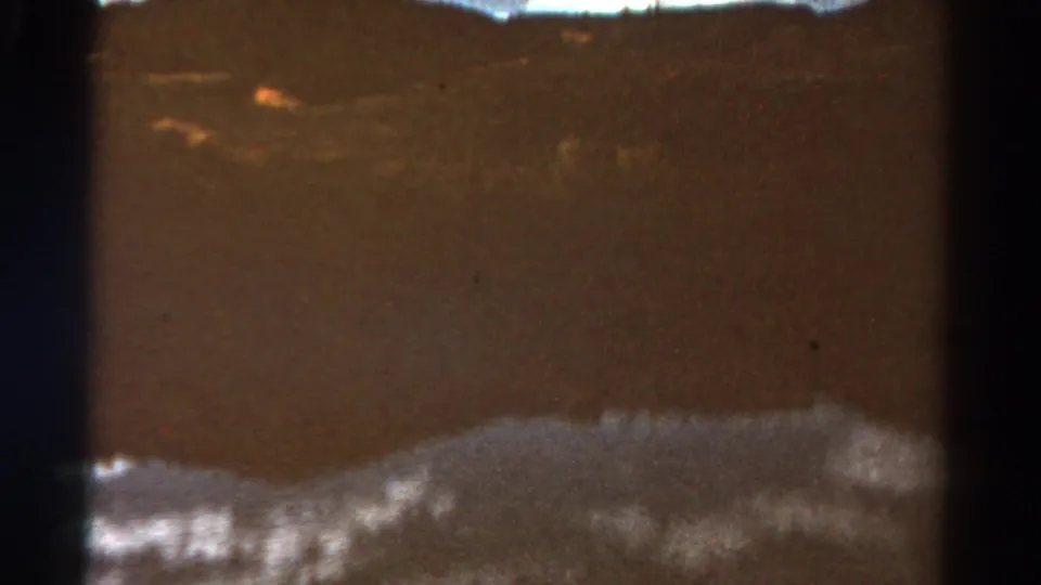 1967 Colorado home-movie still showing a muted water surface, bright shoreline texture, and low hills in soft 8mm color.