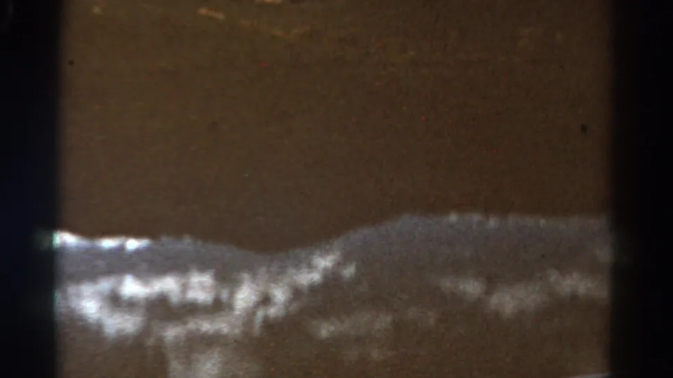 1967 Colorado 8mm frame with still water, a low hillside, bright shoreline highlights, and aged film texture.