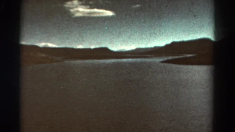 1967 Colorado 8mm frame showing a broad river or reservoir with distant mountains, low clouds, and projected film borders.