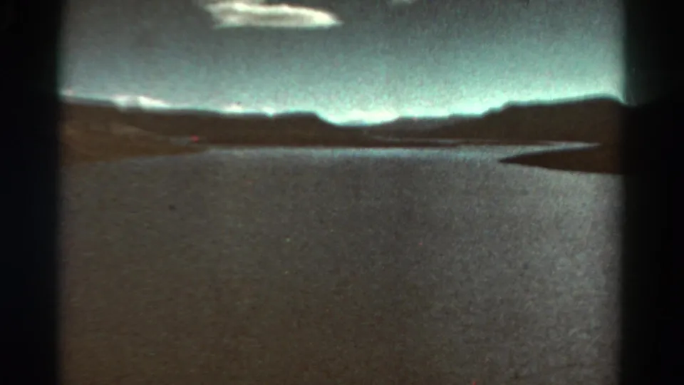 1967 Colorado 8mm view of a calm river or reservoir bordered by low mountain ridges and a dark right-side shoreline.