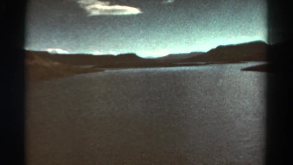 1967 Colorado 8mm landscape showing bright water, dark mountain ridges, scattered clouds, and the rounded edges of projected film.