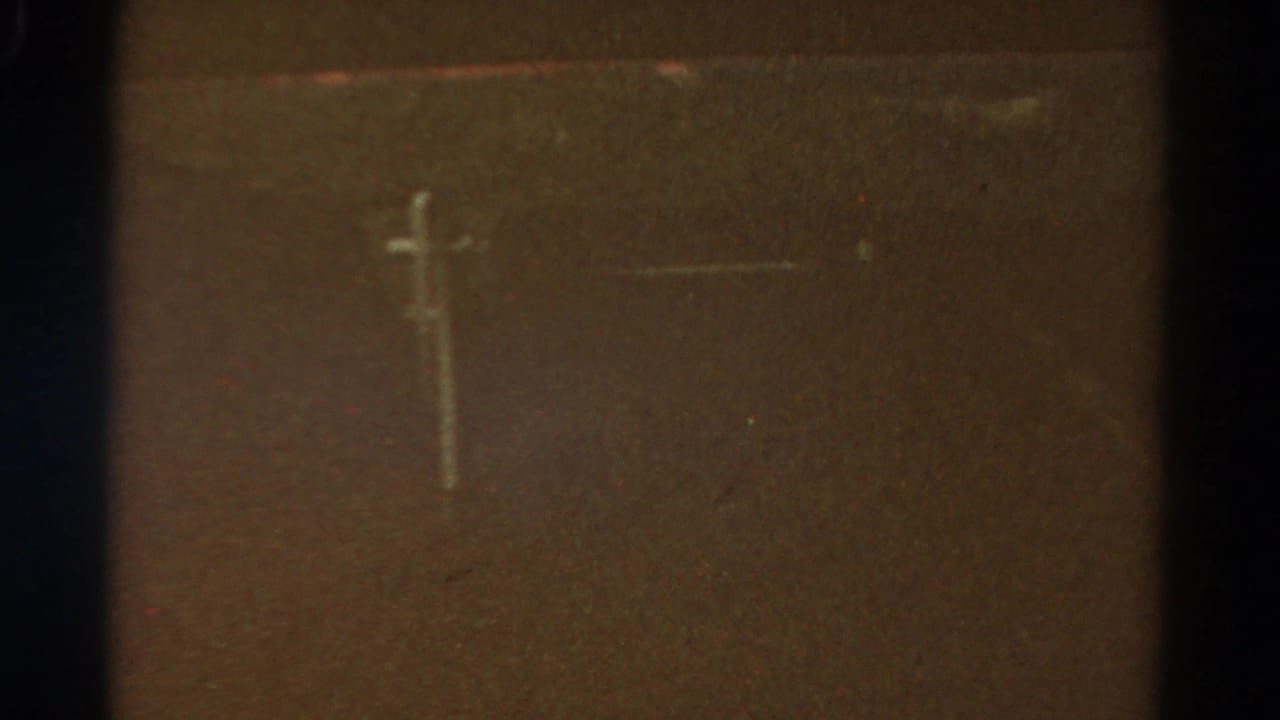 Dim roadside utility pole seen through grainy 8mm film with dark frame edges.