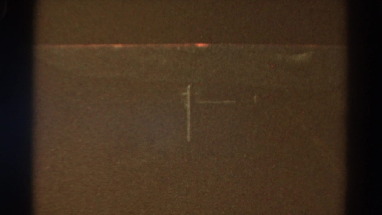 Faint utility pole and crosshair mark against a dark brown roadside view.