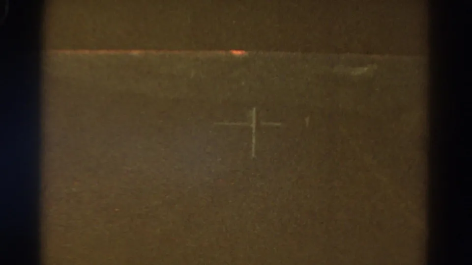 The moving 8mm frame shows a central crosshair-like mark, dark gate edges, and muted roadside tones from 1967 Colorado footage.