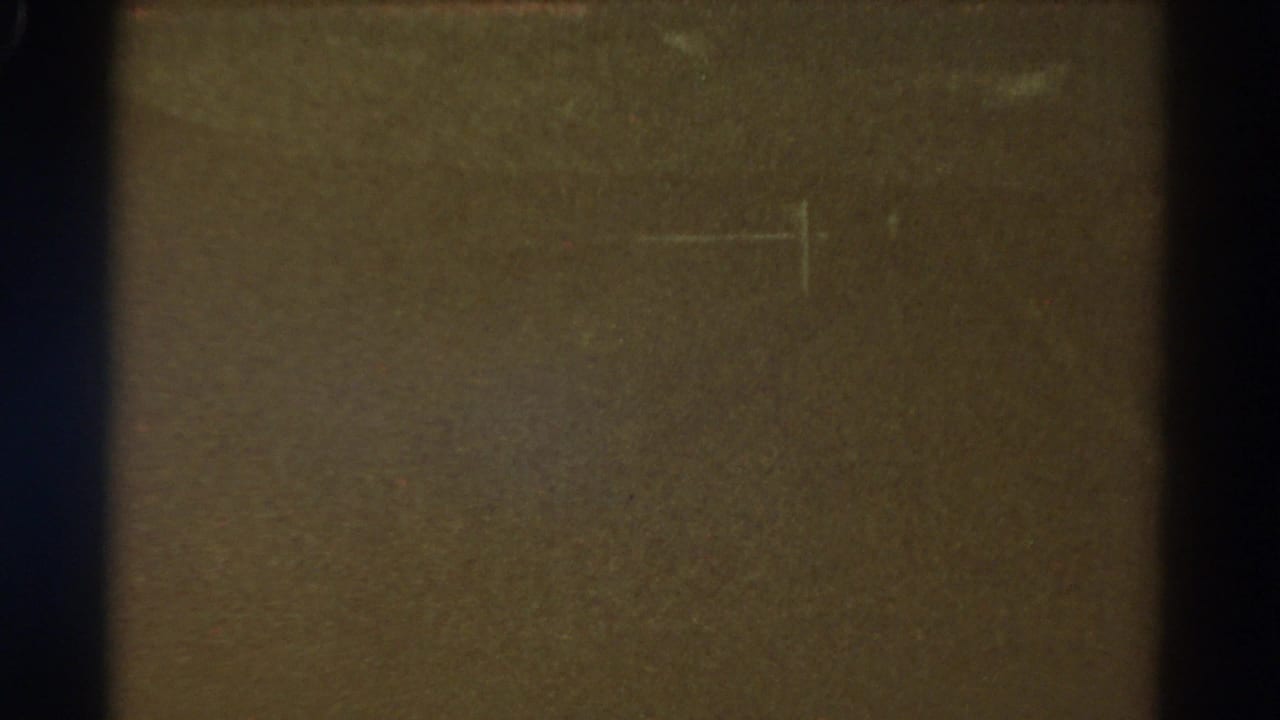 Dark underexposed 1967 Colorado 8mm frame with brown-black tone, visible film edge, dust, grain, and faint scratch marks.
