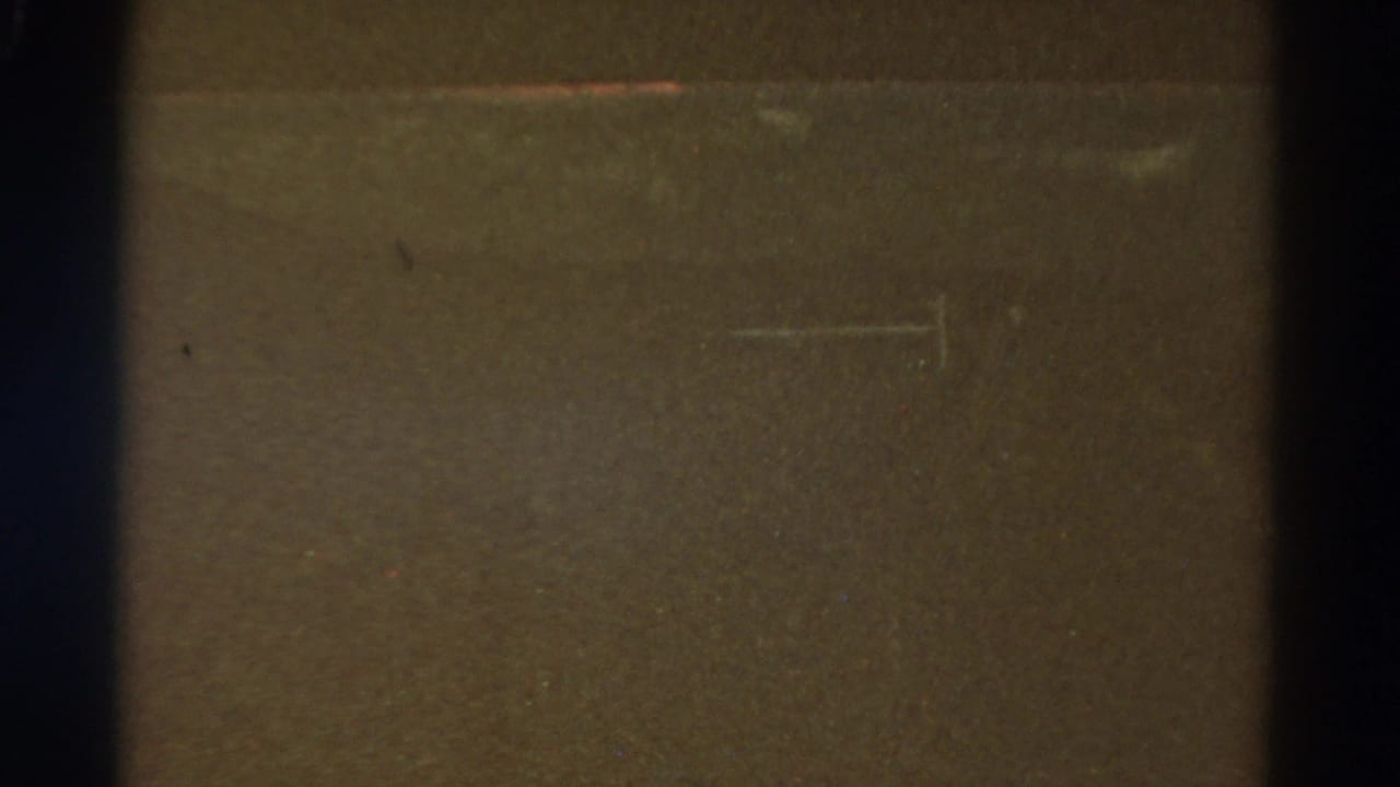 Obscured 1967 Colorado 8mm frame showing a central dark divider, brown-black exposure, fine grain, dust, and light scratch marks.