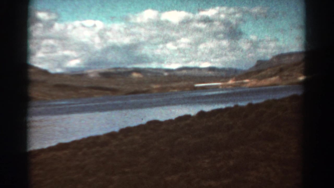 Lake shoreline, brown hills, and distant mountains framed by dark 8mm film edges.