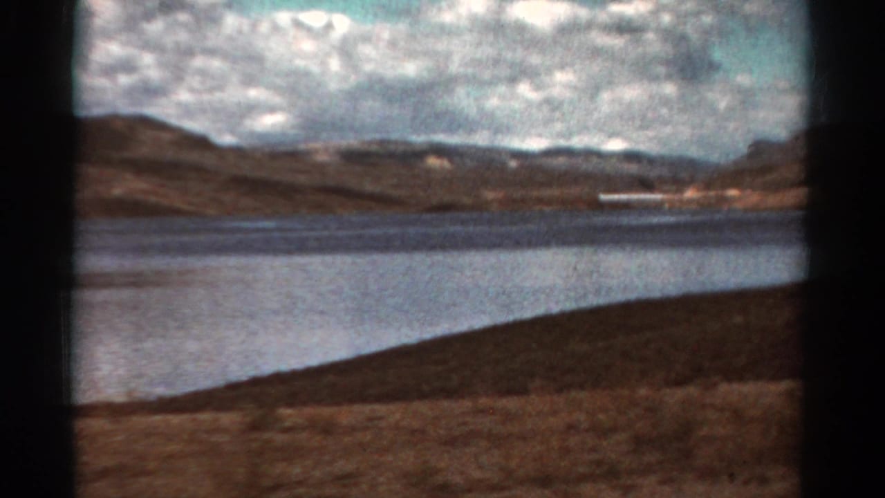 Wide lake view with hills and a long white structure on the far shoreline.