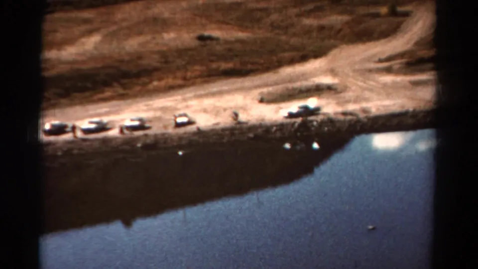 1967 Colorado 8mm frame with classic cars parked near a lake, a pale dirt road, dry hills, and dark film borders.