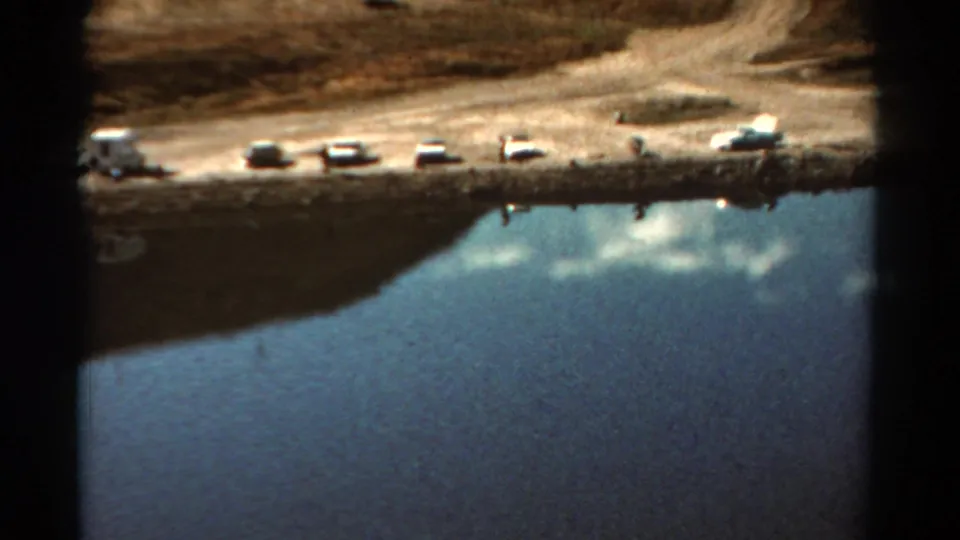 Final 1967 Colorado frame with a row of cars, small lakeside figures, dirt shore, and calm reflective water.