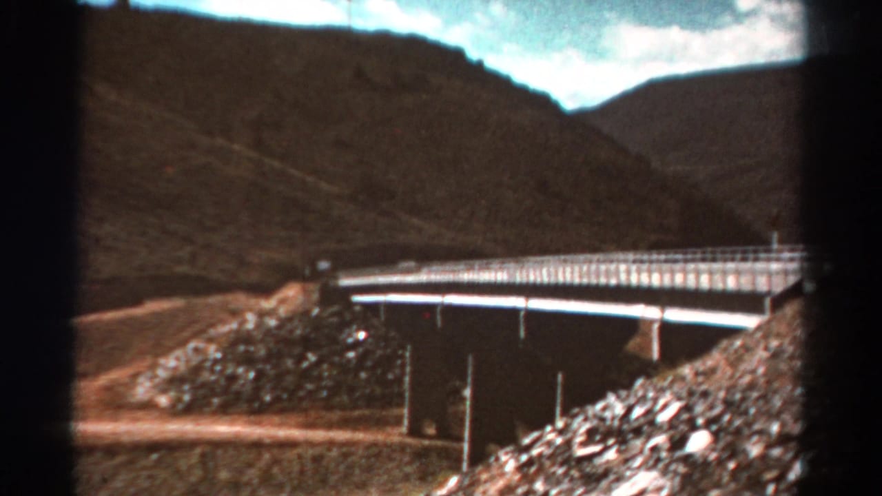 Bridge spans a rocky drainage with hills rising behind it.