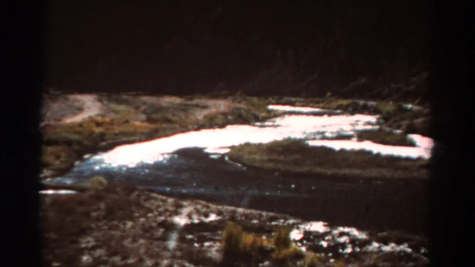 Vintage 8mm view of a shallow Colorado river or stream reflecting light through a rugged valley.